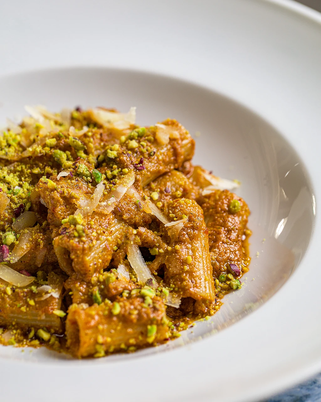 Rigatoni nappés de sauce crémeuse, parsemés de pistaches concassées et de copeaux de fromage