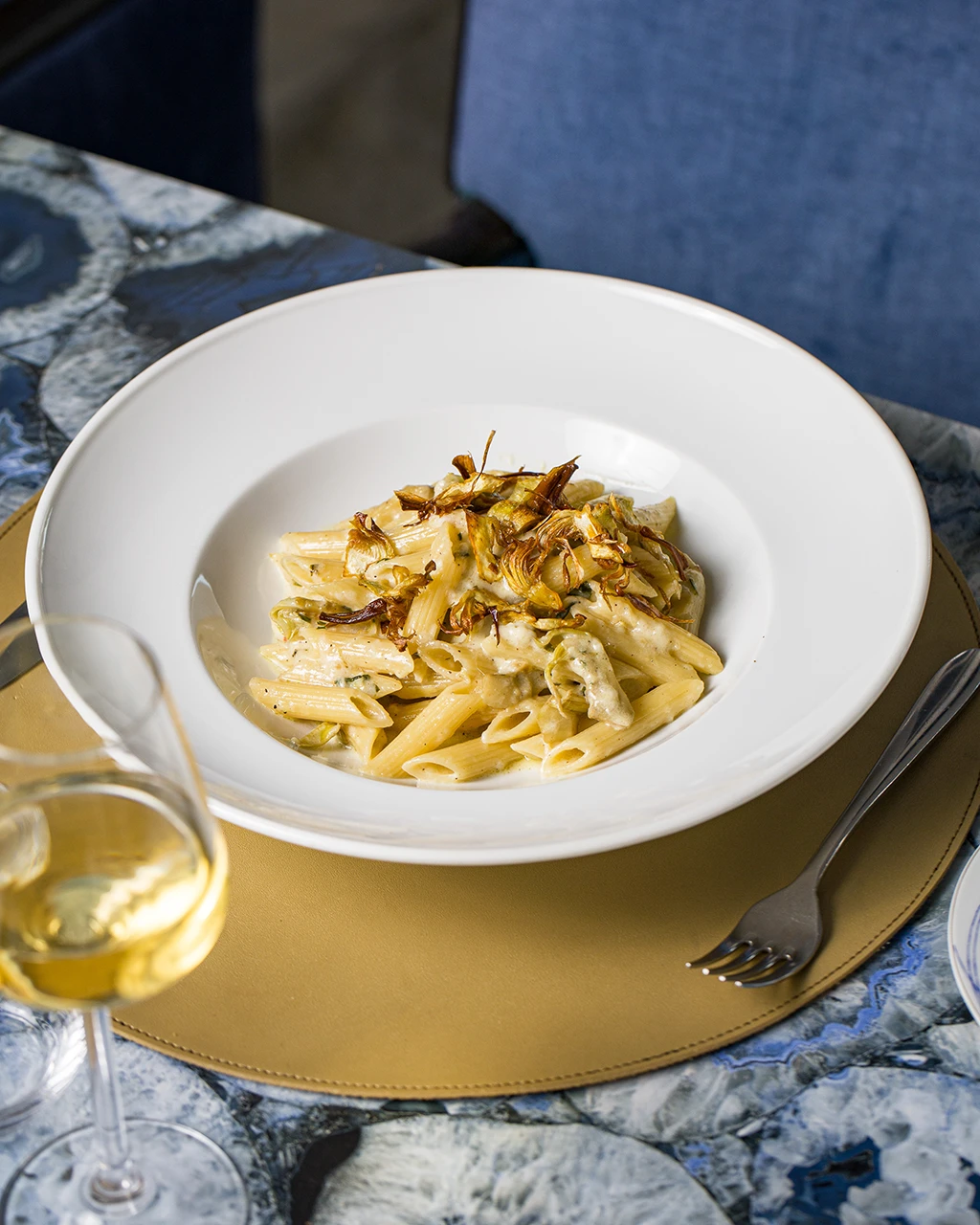 Penne à la crème et artichauts croustillants dans une assiette creuse, verre de vin blanc à côté