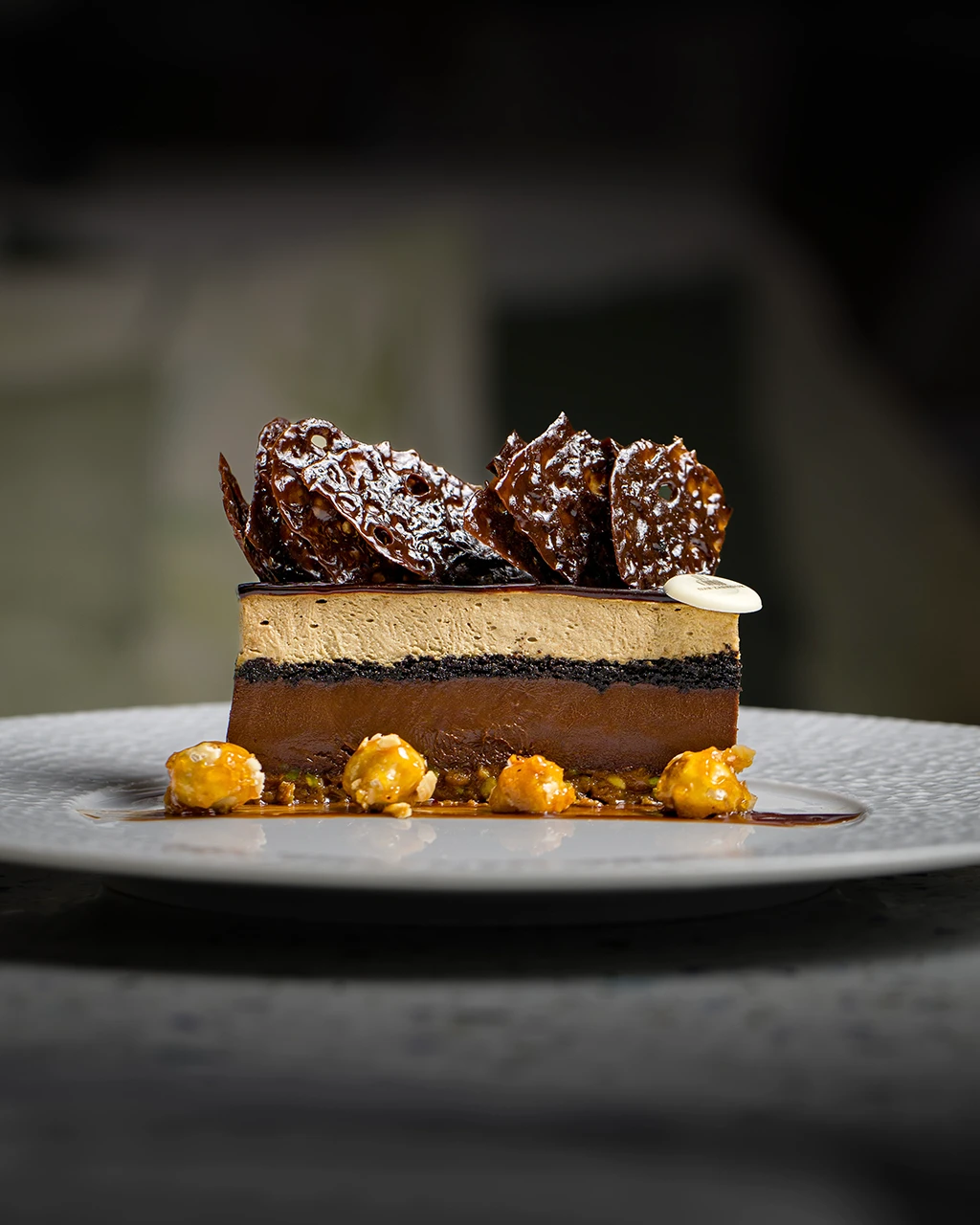 Entremets au chocolat en couches, orné de tuiles croustillantes au caramel et de noix caramélisées