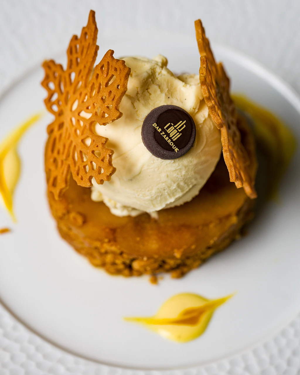Gâteau doré surmonté d’une boule de glace vanille et de dentelles croustillantes, au logo Dar Zarrouk