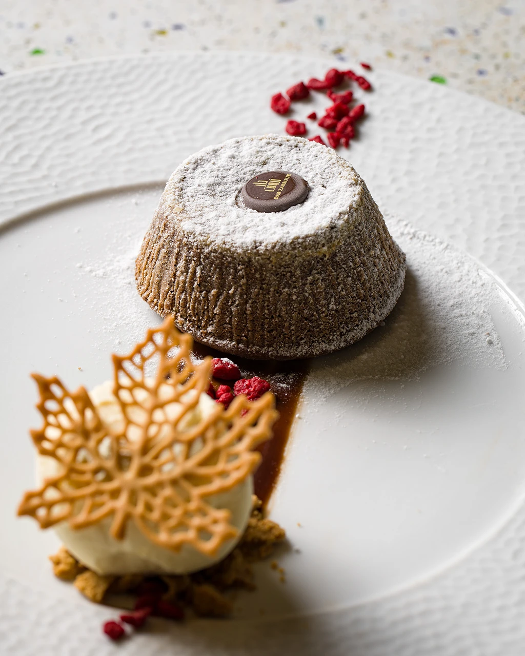 Fondant au chocolat saupoudré de sucre glace, avec une quenelle de crème et une dentelle croustillante