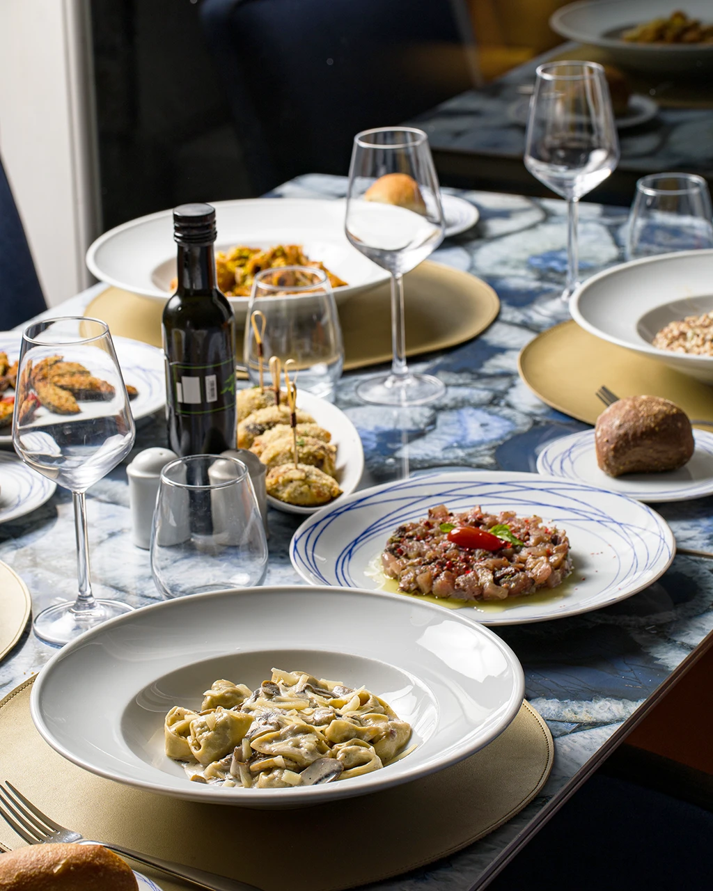 Table dressée avec tortellinis aux champignons, tartare, bouchées croustillantes, pain et verres