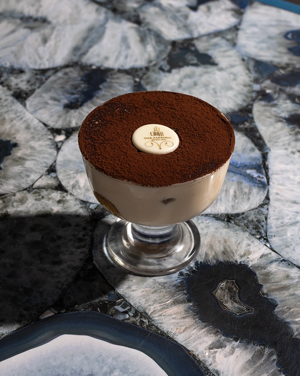 Tiramisu saupoudré de cacao dans une coupe en verre, sur une table en agate bleue