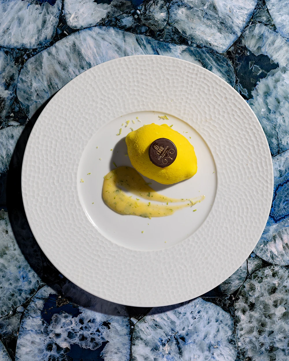 Dessert en forme de citron avec coulis jaune, dressé sur une assiette blanche martelée