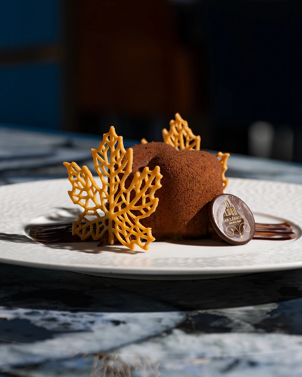 Dessert au chocolat orné de feuilles d’érable en caramel et d’un médaillon Dar Zarrouk
