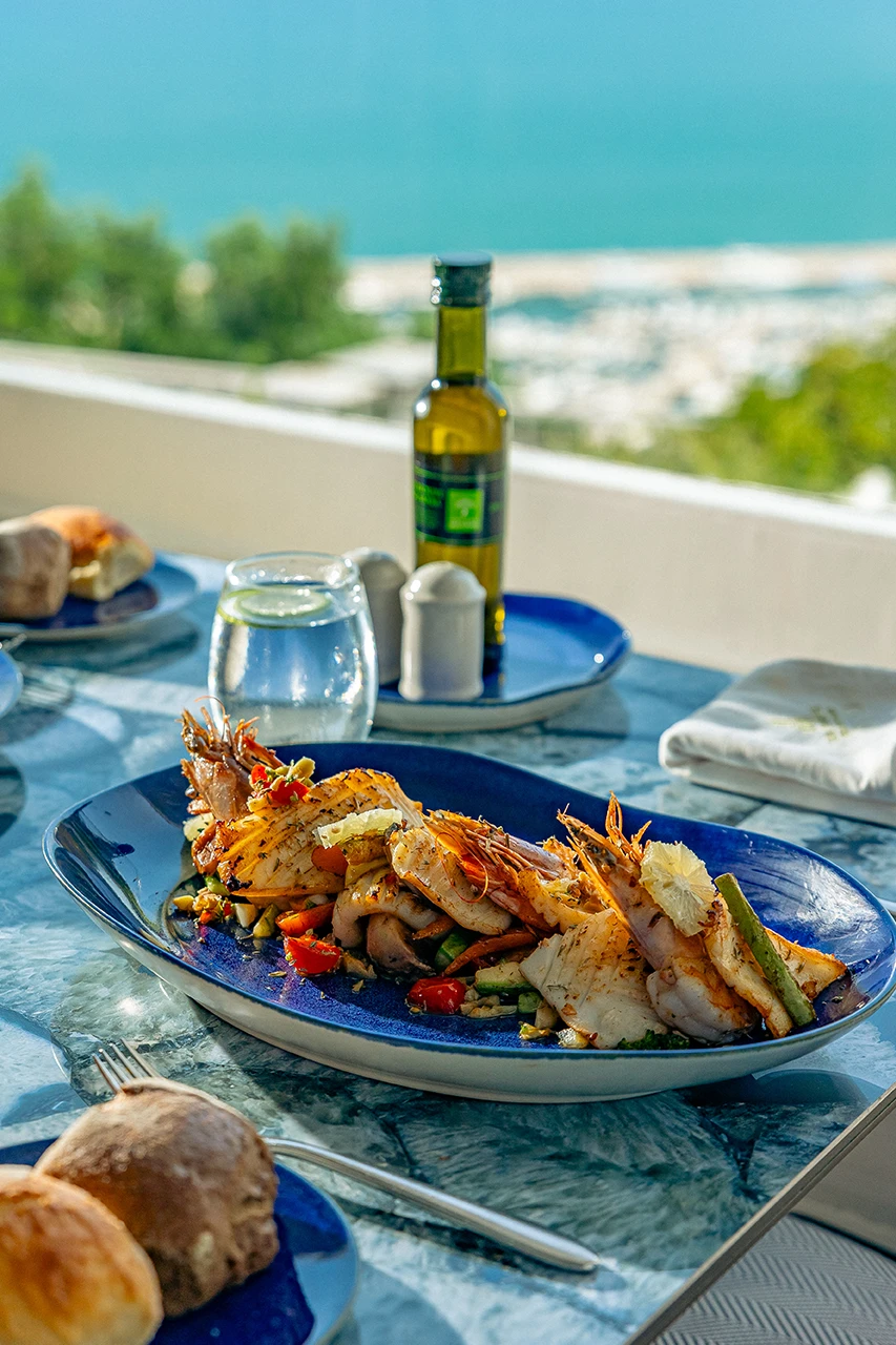 Plat de poissons et crevettes grillés avec légumes, sur une table en terrasse face à la mer