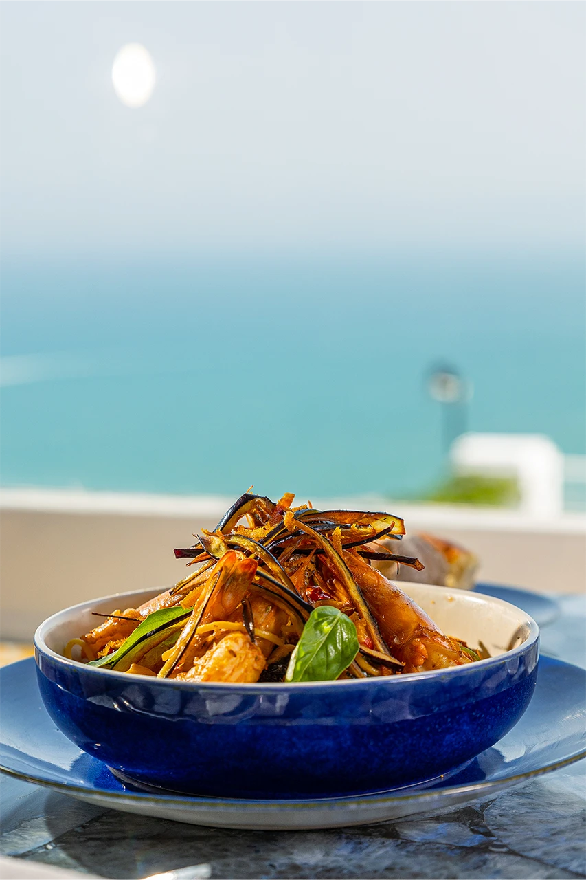 Bol de pâtes aux crevettes et aubergines frites, avec la mer en arrière-plan