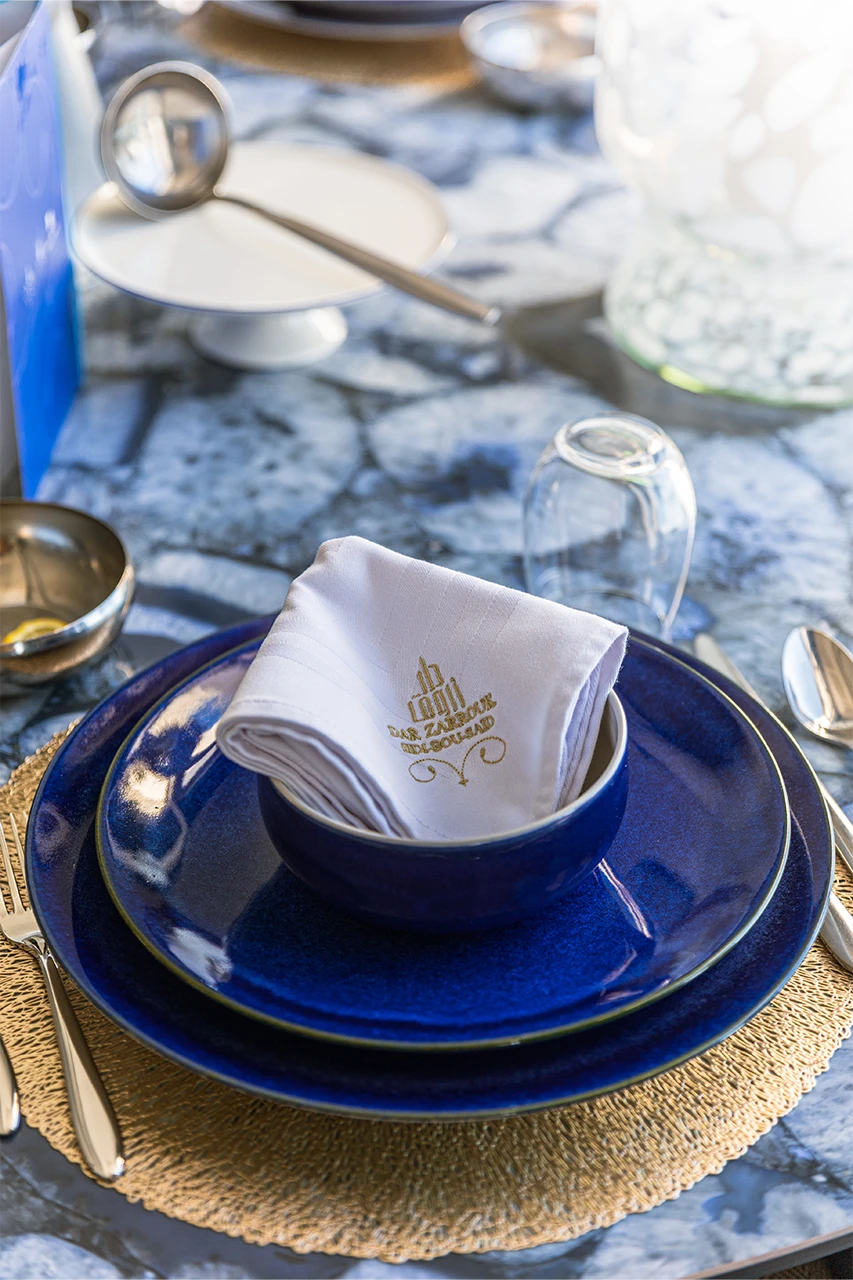 Assiettes bleues superposées avec serviette brodée Dar Zarrouk sur un set de table doré
