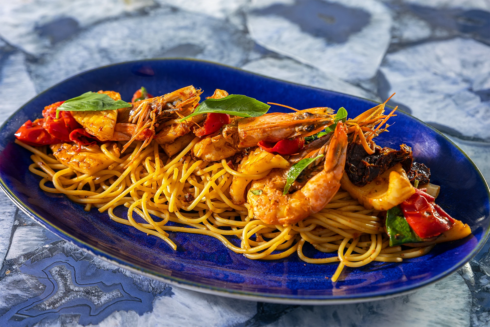 Spaghettis aux crevettes, calamars et tomates séchées servis sur un plat bleu