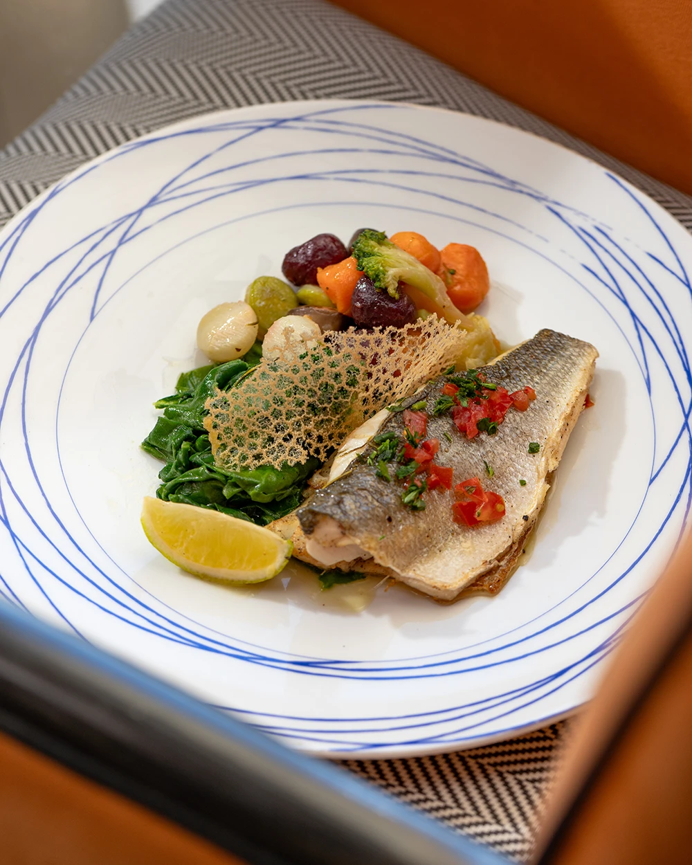 Filet de poisson doré aux épinards, légumes glacés et citron, dans une assiette à filets bleus