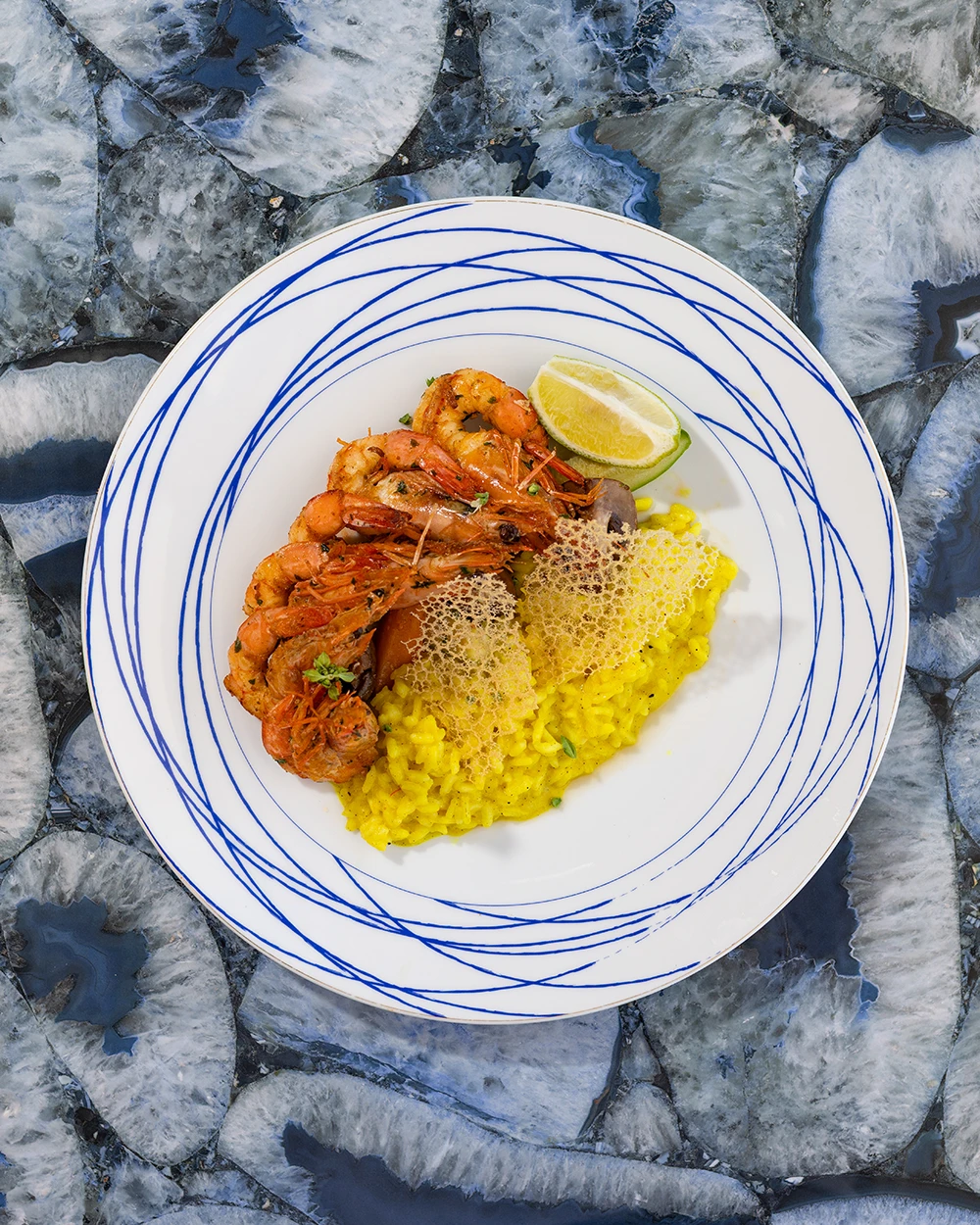 Gambas grillées sur riz safrané, croustillant de fromage et citron vert, assiette bleue et blanche